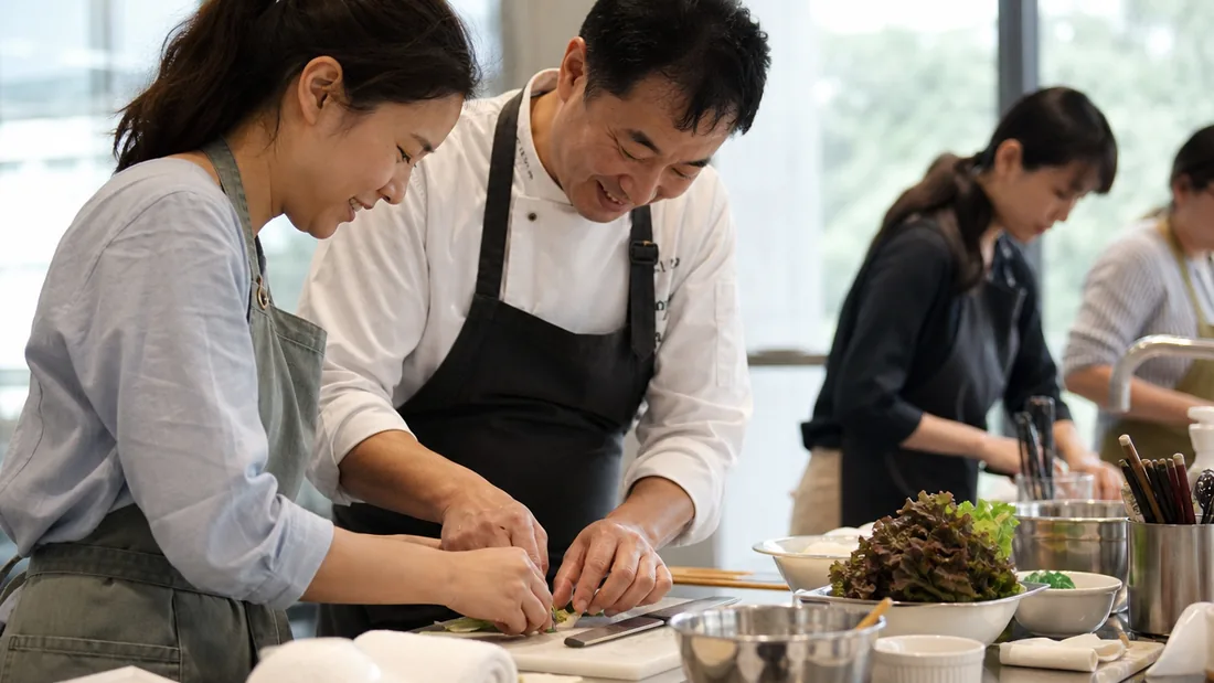 A chef guiding a beginner through a hands-on cooking step at a one day class in Singapore