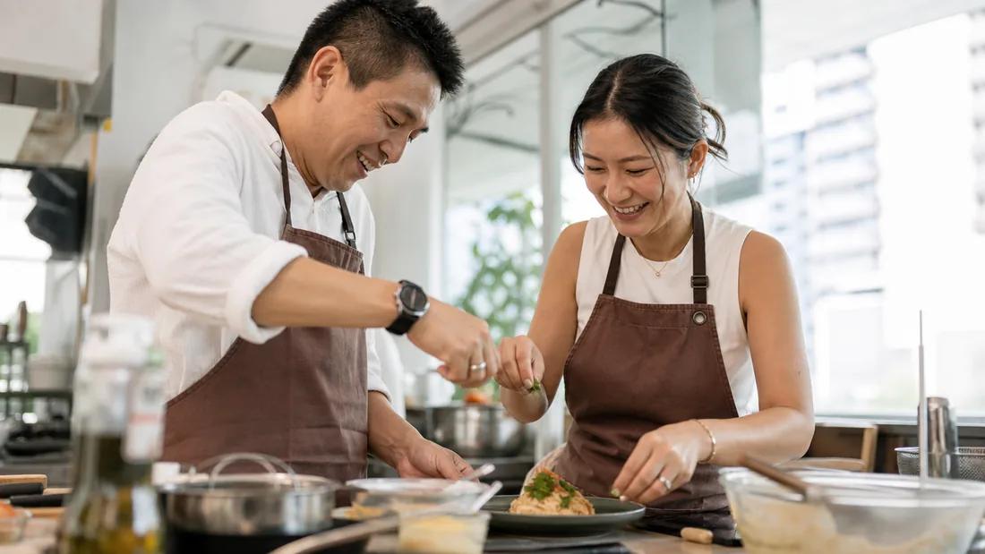 Two people cooking side by side and plating a finished dish at a short class in a Singapore studio