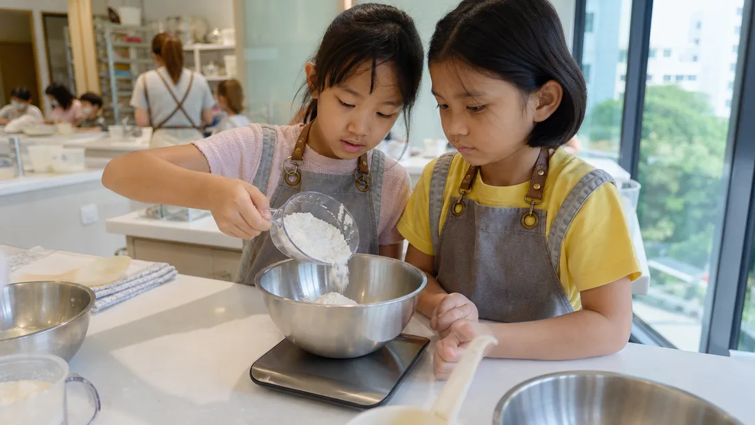 Young children measuring flour and mixing batter together at a guided baking workshop