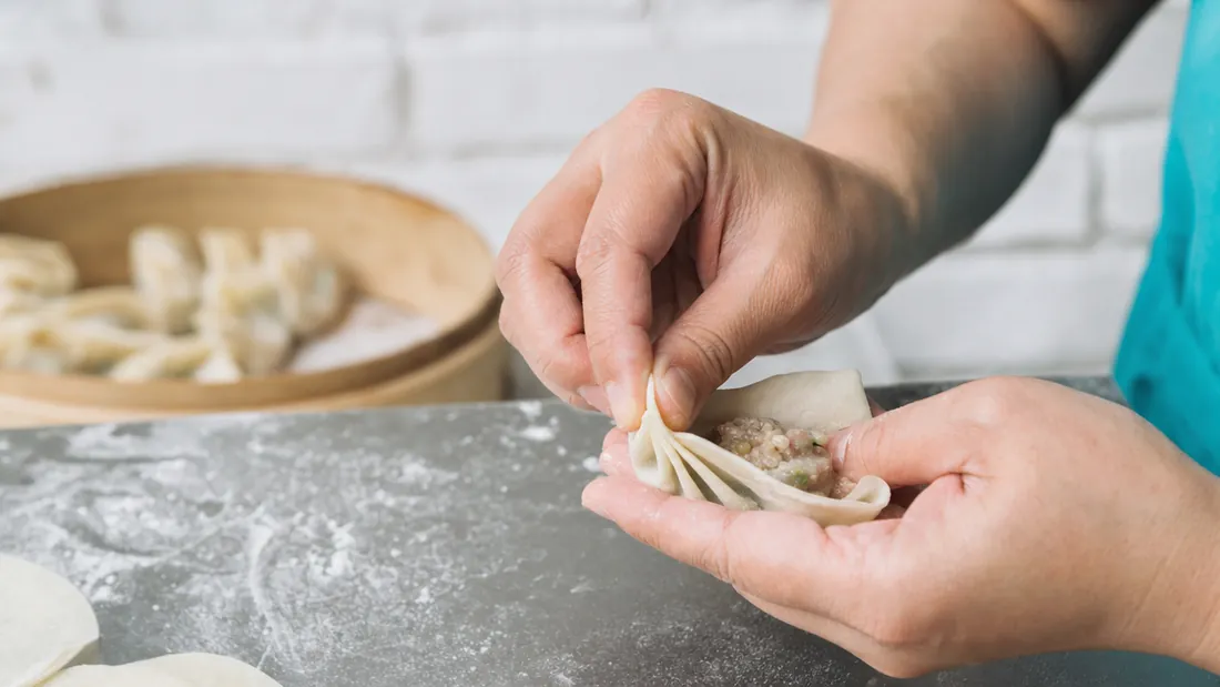 Close-up of hands pleating a dumpling wrapper at a bao making class in Singapore