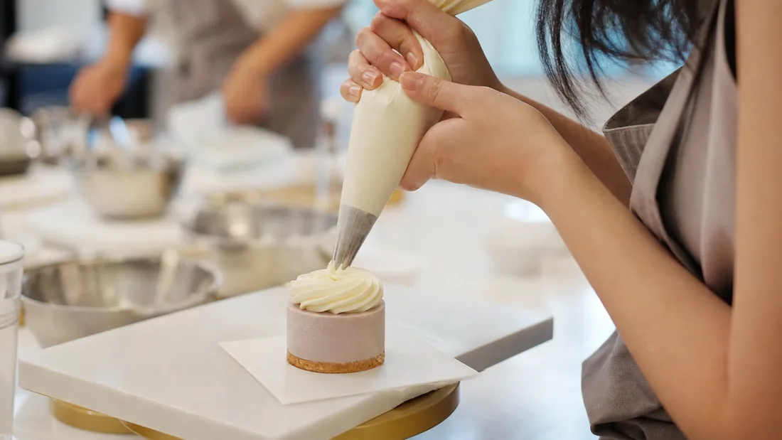 Close-up of hands piping buttercream onto a dessert at a workshop in Singapore