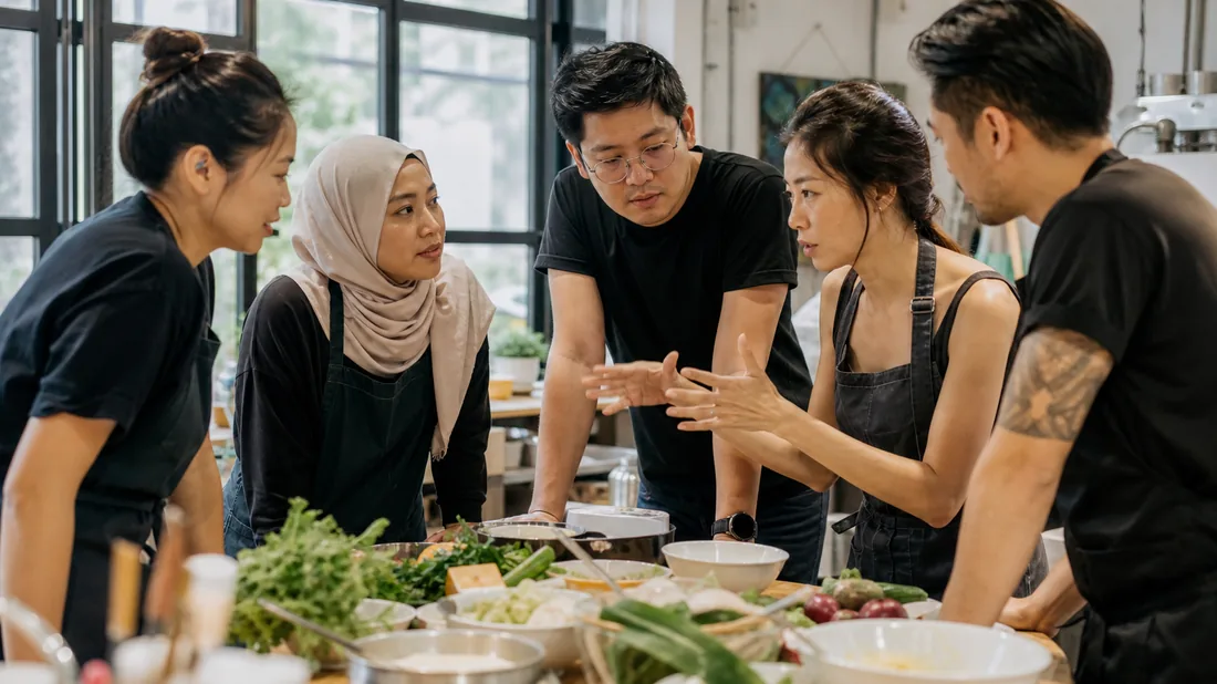 A cooking team building group in Singapore huddled in strategy mode around their mystery box ingredients