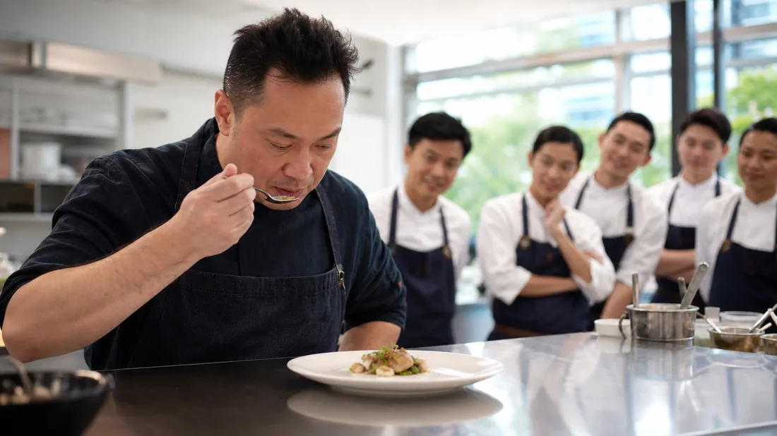 A chef tasting and evaluating a team's dish at a competitive cooking team building challenge in Singapore