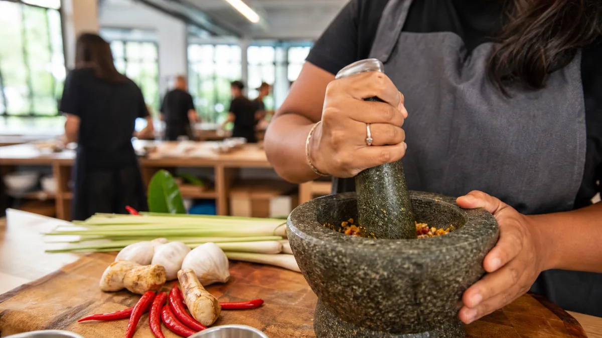 Hands pounding fresh Thai curry paste in a stone mortar at a bright Singapore cooking studio